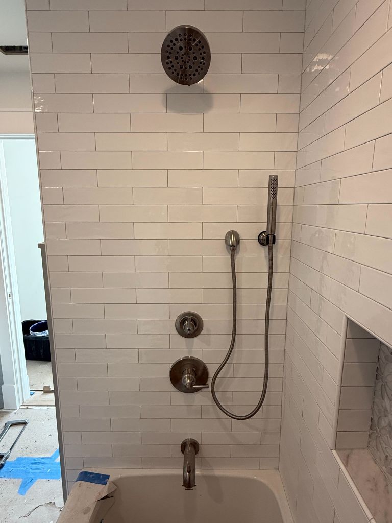 Subway tile shower enclosure with brushed metal fixtures and handheld wand