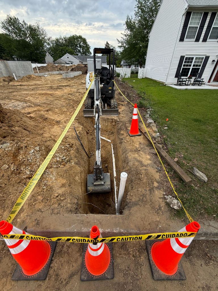 Mini excavator in deep sewer trench with caution tape