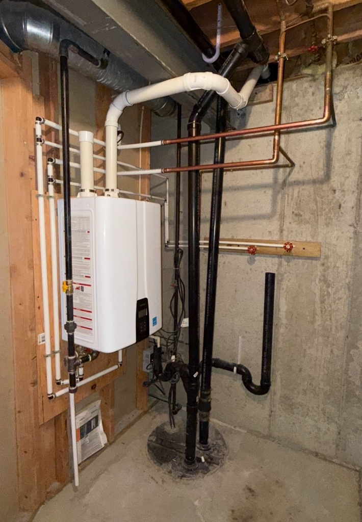 Navien tankless water heater installed in basement with copper supply lines and PVC venting
